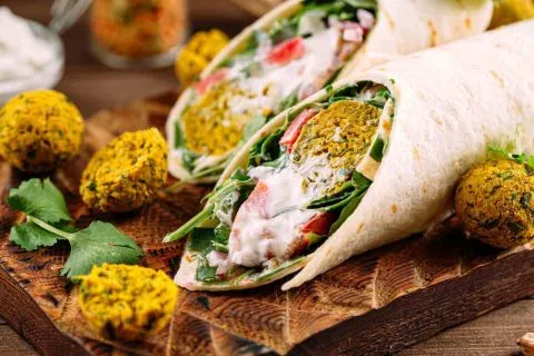 Crispy baked falafel wraps filled with fresh greens, tomatoes, and creamy tahini sauce, served with extra falafel on the side.